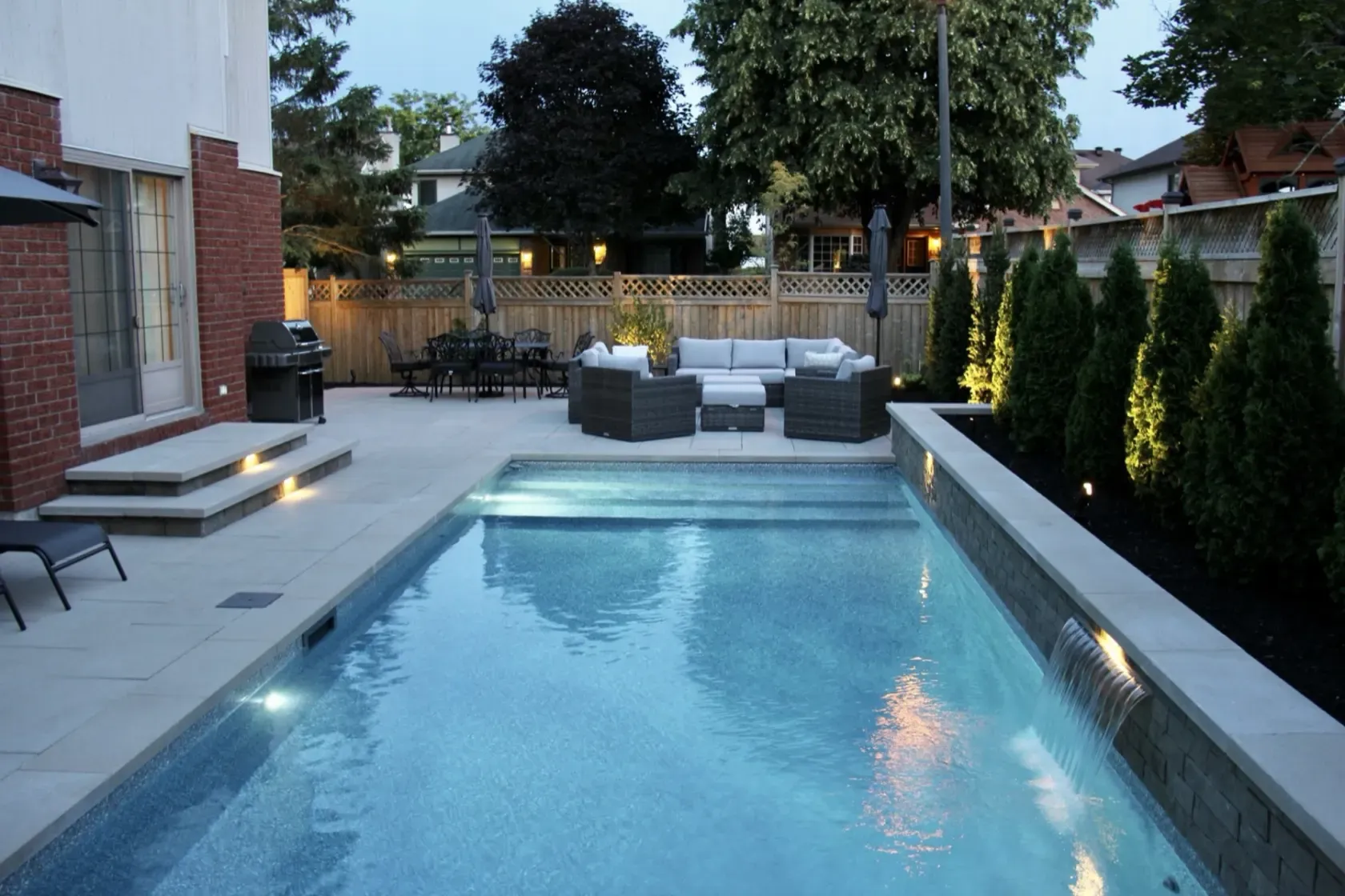 Illuminated pool and backyard at dusk
