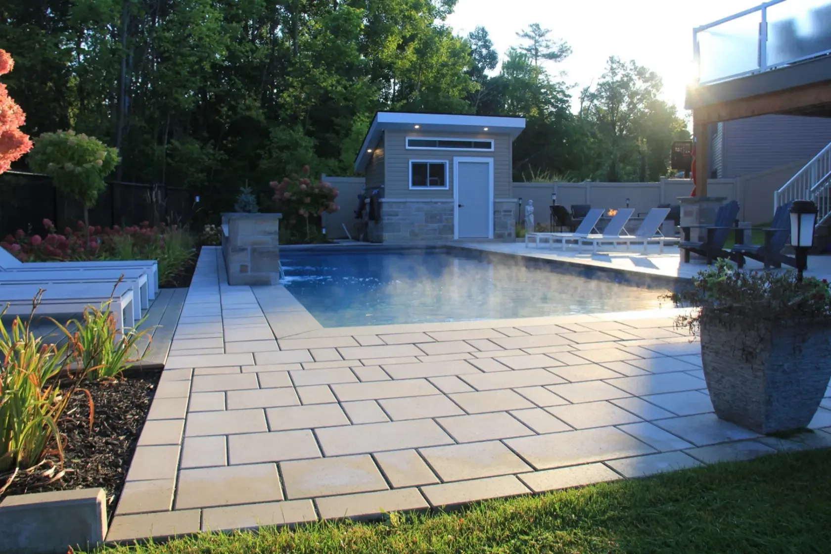 Completed pool, stone patio and modern pool house in a professionally landscaped backyard